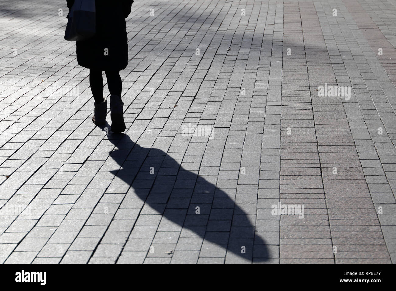 Schlanke Mädchen auf der Straße, schwarze Schatten und Silhouette am Bürgersteig. Frau in warme Kleidung outdoor, Konzept der Einsamkeit, der dramatischen Geschichte Stockfoto