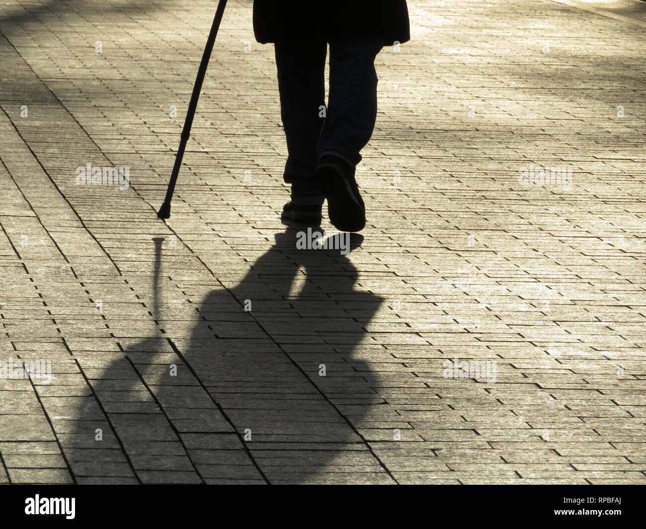 Silhouette der Mann mit einem Stock, lange Schatten auf Pflaster. Konzept der blinden Person, hinkend, Behinderung, Alter, Erkrankungen der Wirbelsäule Stockfoto