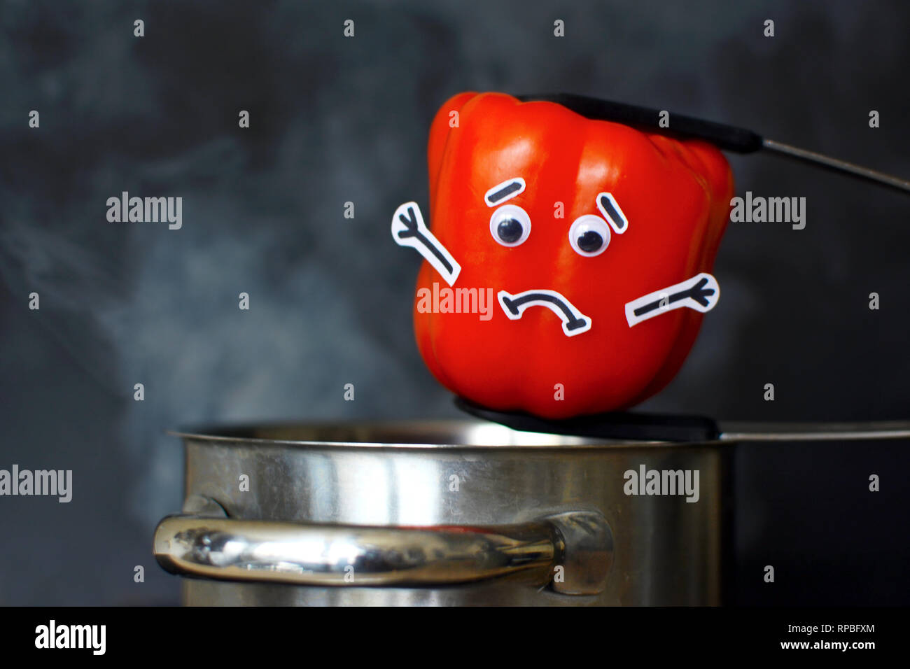 Rote Paprika mit einem traurigen Gesicht in einem dampfenden Kochtopf auf dunklen schwarzen Hintergrund gesetzt werden Stockfoto