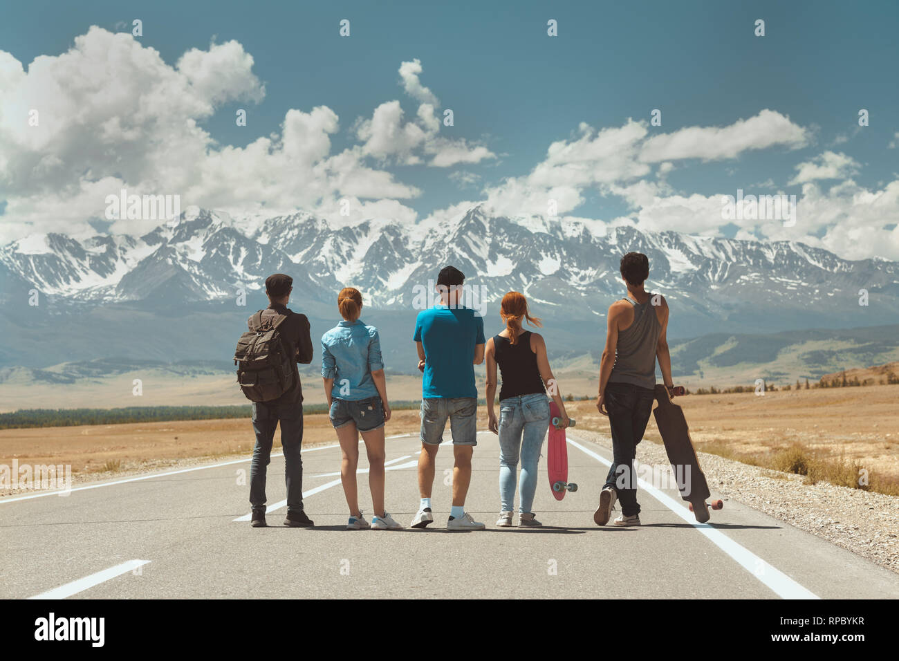Eine Gruppe von fünf Freunden steht auf langen geraden Straße und blickt auf die Berge. Travel Concept Stockfoto