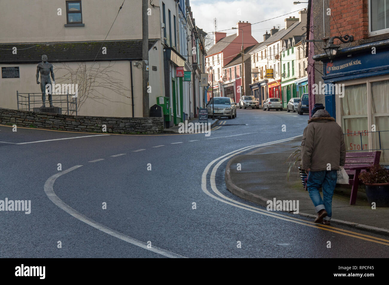 Ein Mann, der Hauptstraße von Ballydehob in West Cork, vorbei an der Statue des lokalen Helden und berühmten Wrestler "Anno'O'Mahony. Stockfoto