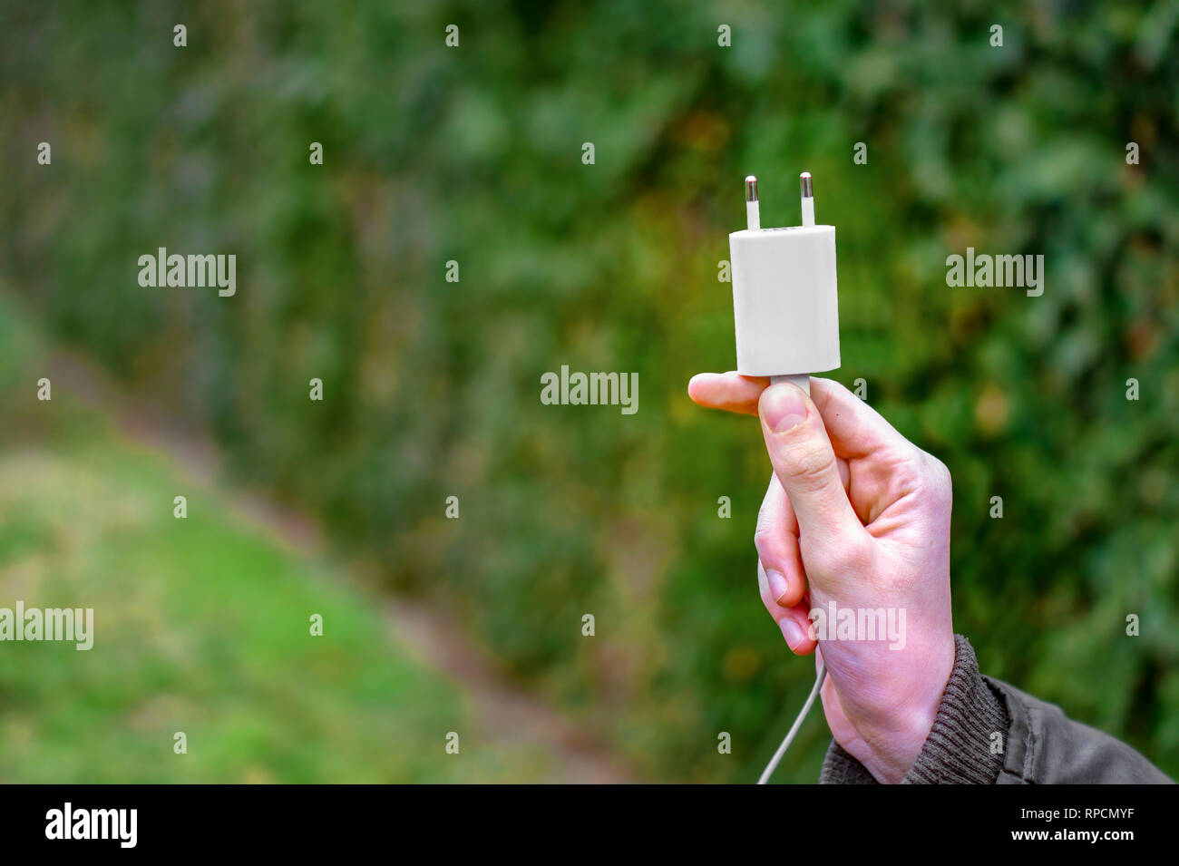 Hand eine unplugged Ladestecker außerhalb Holding in die grüne Natur - die Natur über die elektronischen Geräte Konzept wählen Stockfoto