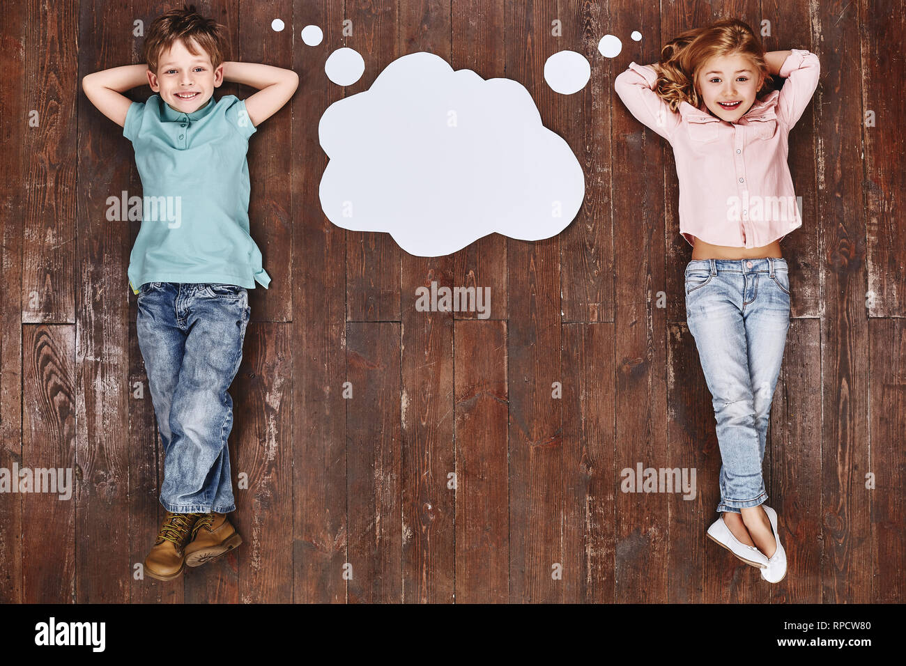 Glückliche Kinder. Ansicht von oben creative Foto des kleinen Jungen und Mädchen auf Vintage Brown Holzboden. Kinder liegen in der Nähe von Leer dachte, Cloud, in die Kamera schauen und lächeln Stockfoto