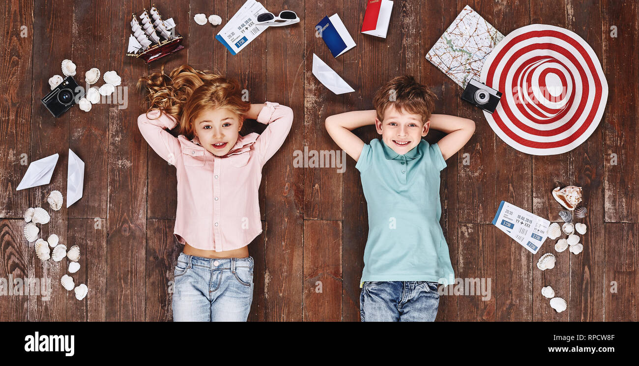 Glückliche Kinder. Ansicht von oben creative Foto des kleinen Jungen und Mädchen auf Vintage Brown Holzboden. Kinder liegen in der Nähe von Reiseutensilien, Kamera und lächelnd Stockfoto
