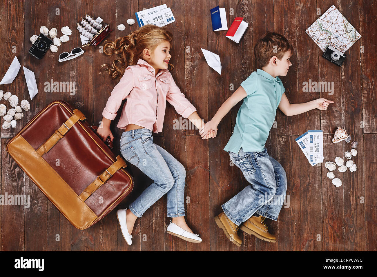 Glückliche Kinder. Ansicht von oben creative Foto des kleinen Jungen und Mädchen auf Vintage Brown Holzboden. Kinder liegen in der Nähe von Reiseutensilien. Mädchen mit Koffer Stockfoto