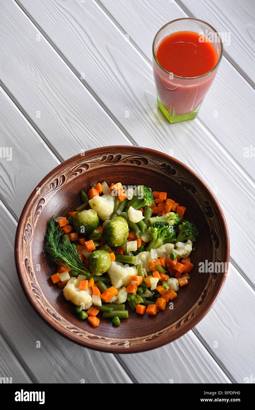 Gemüseragout aus Blumenkohl, Brokkoli, Möhren, Rosenkohl, Erbsen und frischem Dill in Ton Teller serviert mit Tomatensaft auf dem weißen Stockfoto