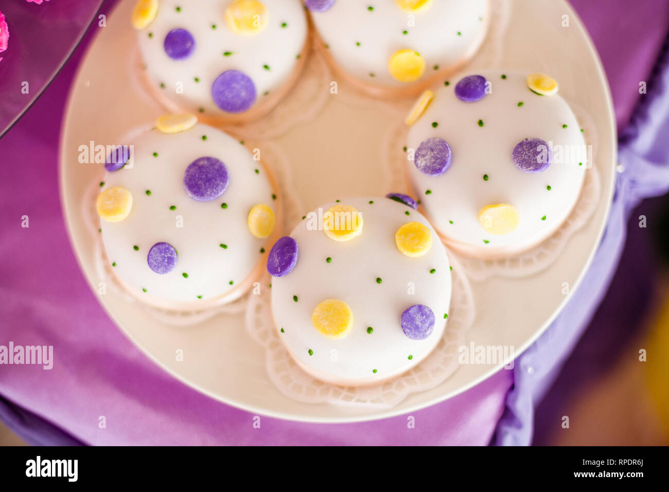 Candy Bar zum Geburtstag. Weiße, runde Kuchen mit großen gelben und violetten Punkten und mit kleinen grünen Punkte. Ansicht von oben Stockfoto