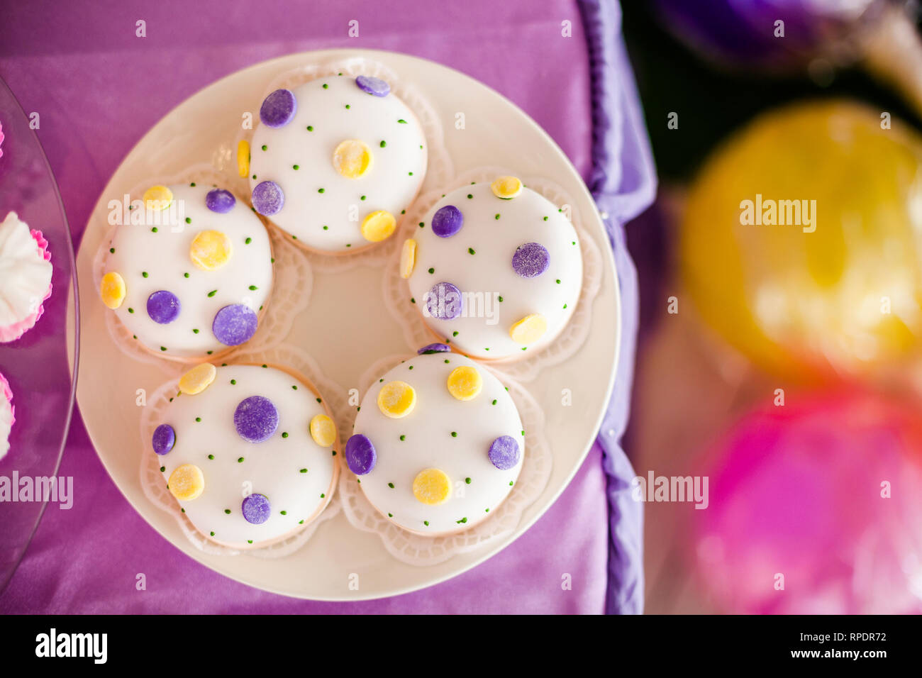 Candy Bar zum Geburtstag. Weiße, runde Kuchen mit großen gelben und violetten Punkten und mit kleinen grünen Punkte. Ansicht von oben Stockfoto