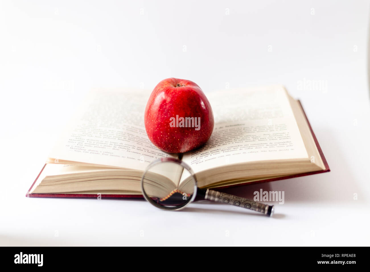 Buch, Lupe und Apfel auf dem Tisch. Das Buch mit dem roten Apfel öffnen. Zum ersten Mal in der Schule. Grundschule. Stockfoto