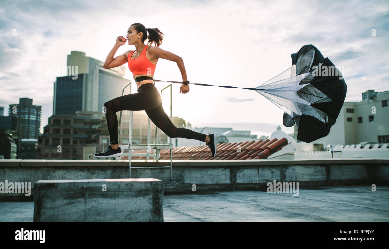 Weibliche Athletin trainiert auf der Terrasse eines Gebäudes mit einem Fallschirm hinter ihr. Fitness-Frau, die hart mit einem Fallschirm auf dem Dach läuft, mit Su Stockfoto