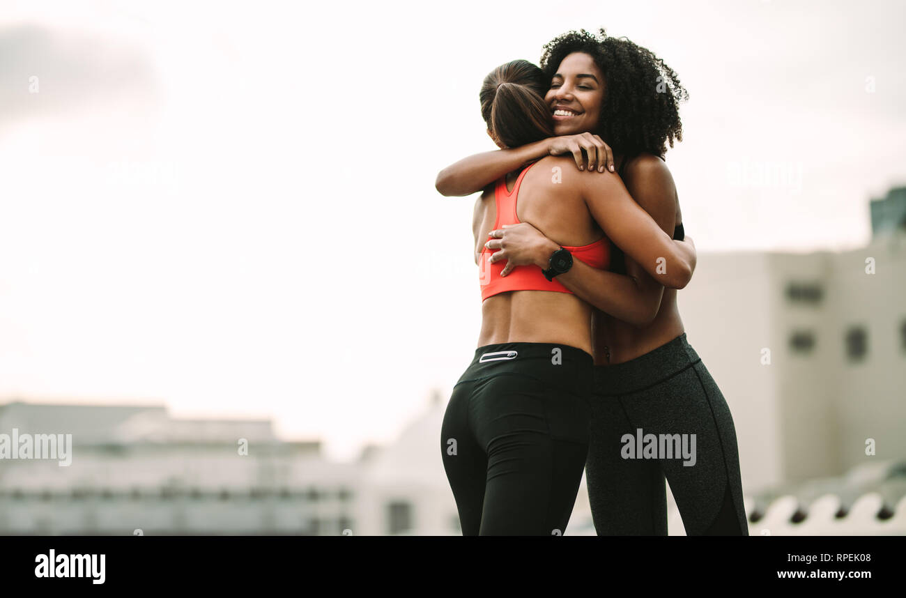Zwei Frauen in Fitnesskleidung umarmen sich beim Workout auf dem Dach. Fitness-Frauen, die sich nach dem Training in Freude umarmen. Stockfoto