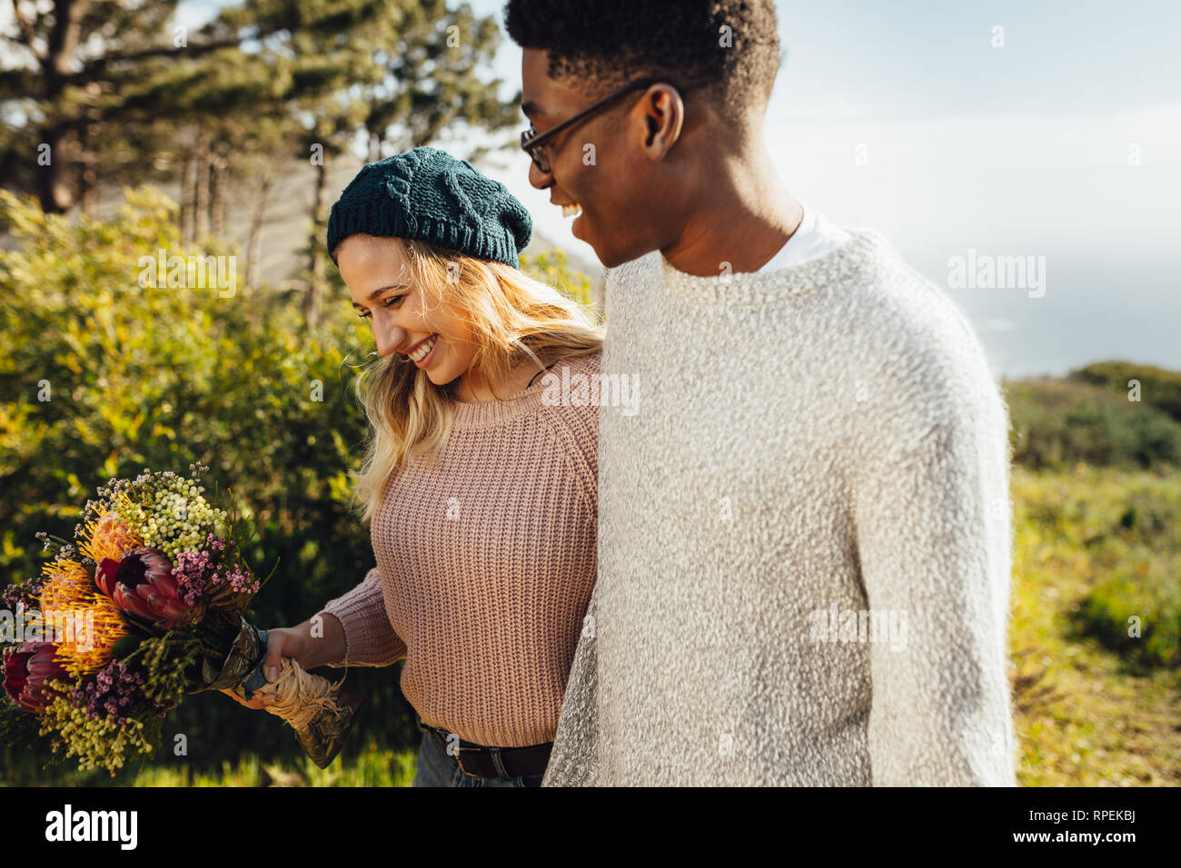 Lächelnde Frau mit Blume zu Fuß mit ihrem Freund im Freien. Paar in Liebe zusammen gehen im Freien. Stockfoto