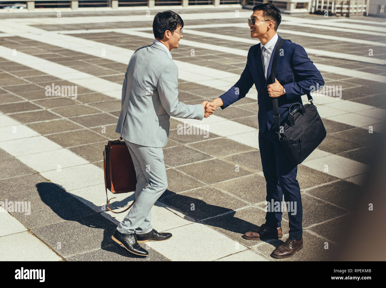 Zwei asiatische Geschäftsleute schütteln draußen in der Stadt die Hand. Geschäftsleute begrüßen sich im Freien. Stockfoto