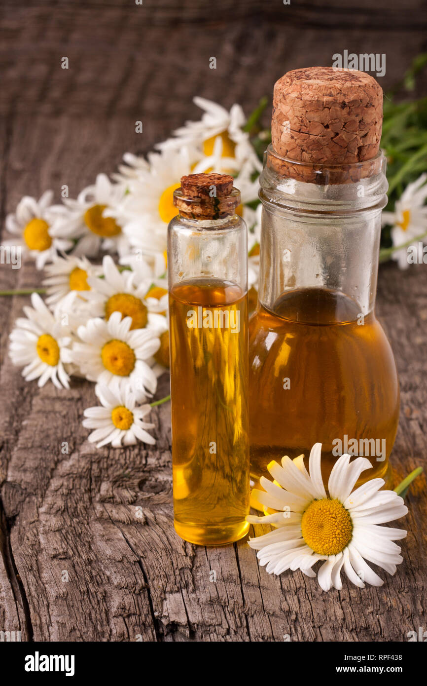 Flasche mit Öl und frische Kamillenblüten auf einer alten hölzernen Hintergrund Stockfoto