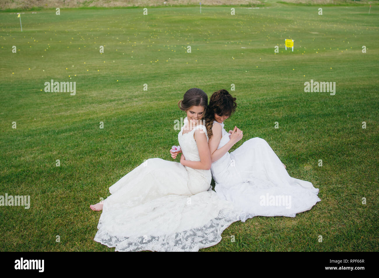 Zwei schöne Bräute Rücken an Rücken sitzen auf den grünen Bereich des Golf Club Stockfoto