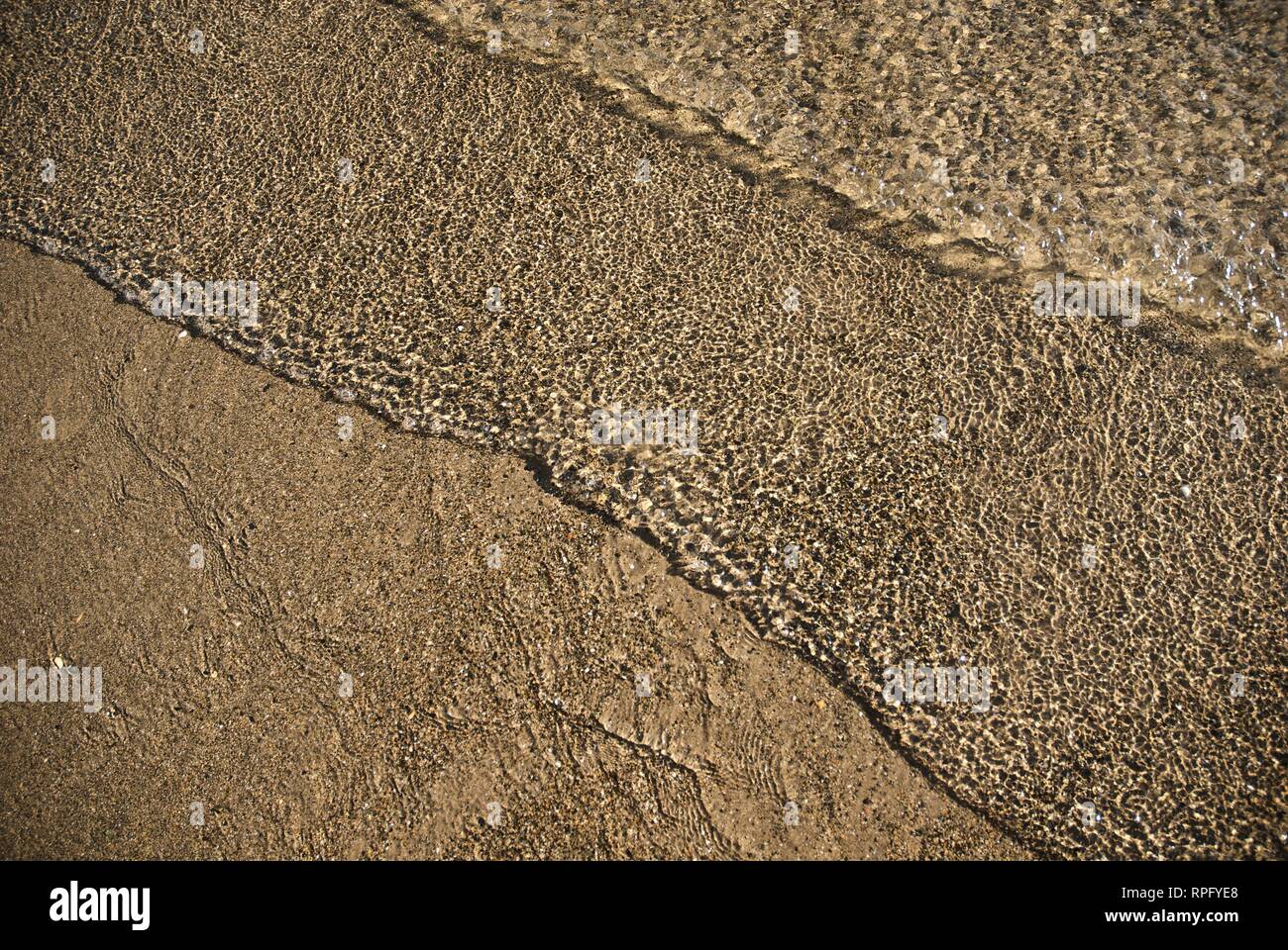 Meer Wasser macht undulating abstrakte Muster und Formen bei strahlendem Sonnenschein, wie es plätschert und wäscht über einen Sandstrand Stockfoto