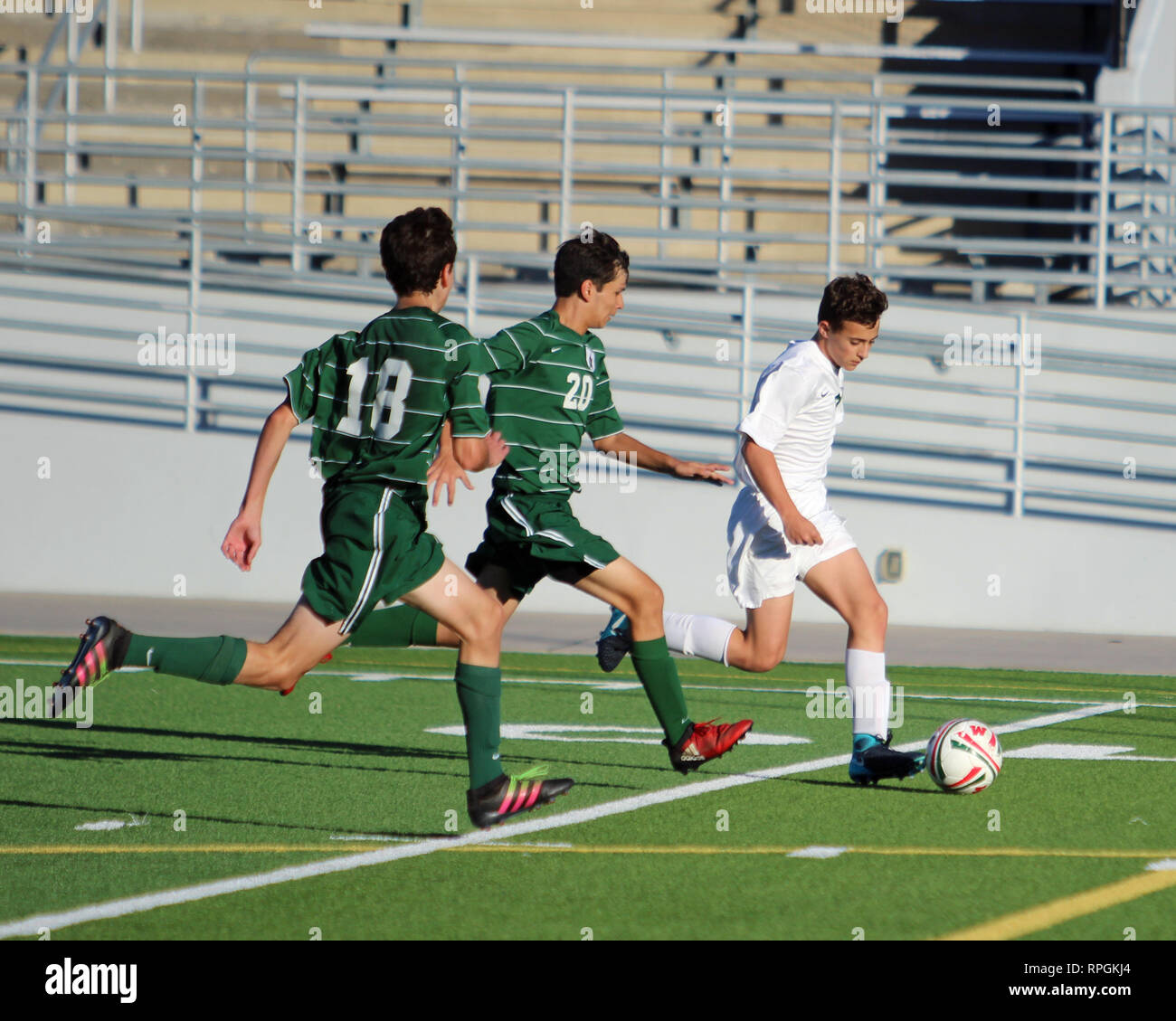 Spieler dribbelt auf der linken Seite des Feldes mit zwei Verteidiger ihn jagen in der High School Jungen Fußball Aktion in Shenandoah, Texas. Stockfoto