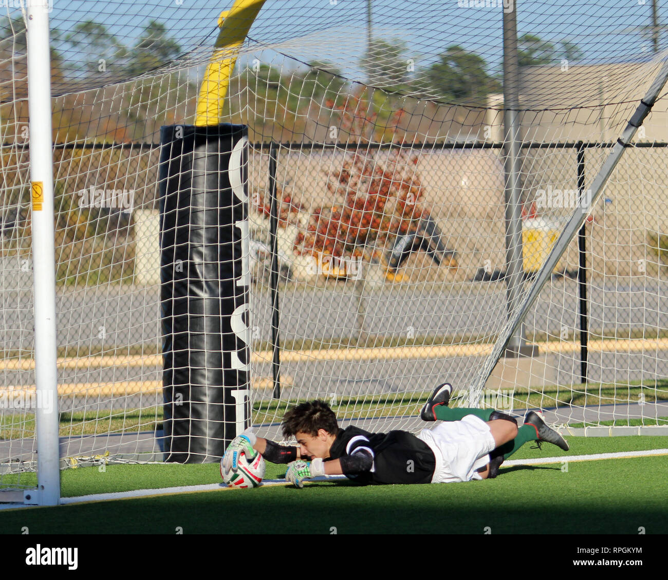 Junge Torwart hält einen Elfmeter mit einem Tauchen sparen, Fang den Ball auf der Torlinie, in der High School Jungen Fußball Aktion in Shenandoah, Texas. Stockfoto