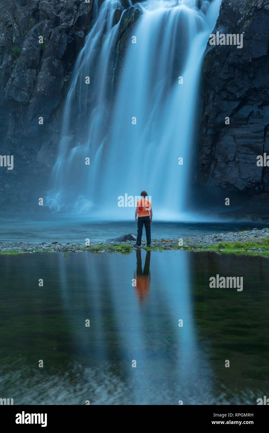 Person reflektiert unter Foss Wasserfall, am Ufer des Fossfjordur. Westfjorde, Island. Stockfoto