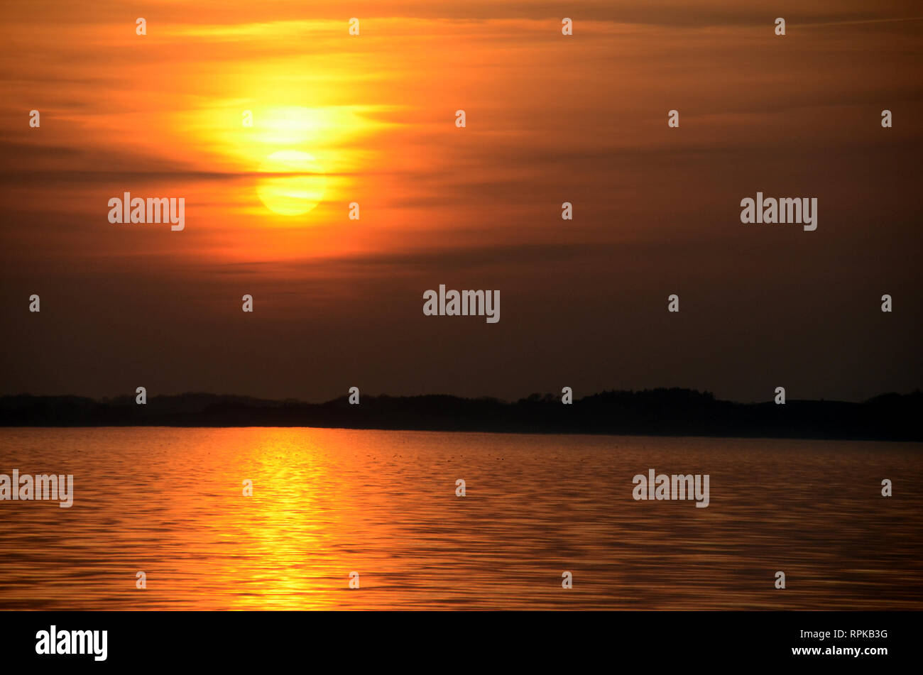 Sonnenuntergang über dem Meer mit einem nebligen Himmel und warmen Farben. Stockfoto