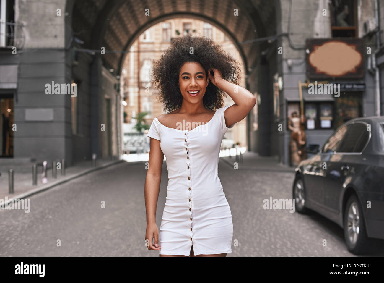 Mühelose Schönheit. Attraktive junge Afro-amerikanische Frau in kurzen weißen Kleid spielen mit Haar und lächelte, während man im Freien Stockfoto