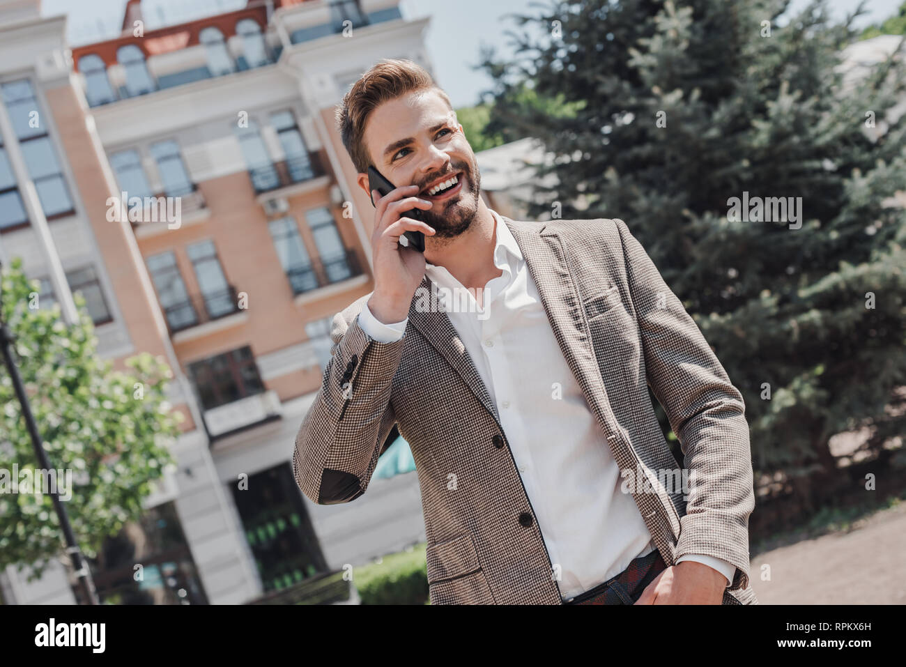 Portrait Of Happy Geschäftsmann Walking im Freien mit Handy. Mann mit Handy. Glückliche Menschen sprechen. Unternehmer im Freien mit Telefon. Er trägt smart casual Outfit der braunen Sakko und weißem T-Shirt. Stockfoto
