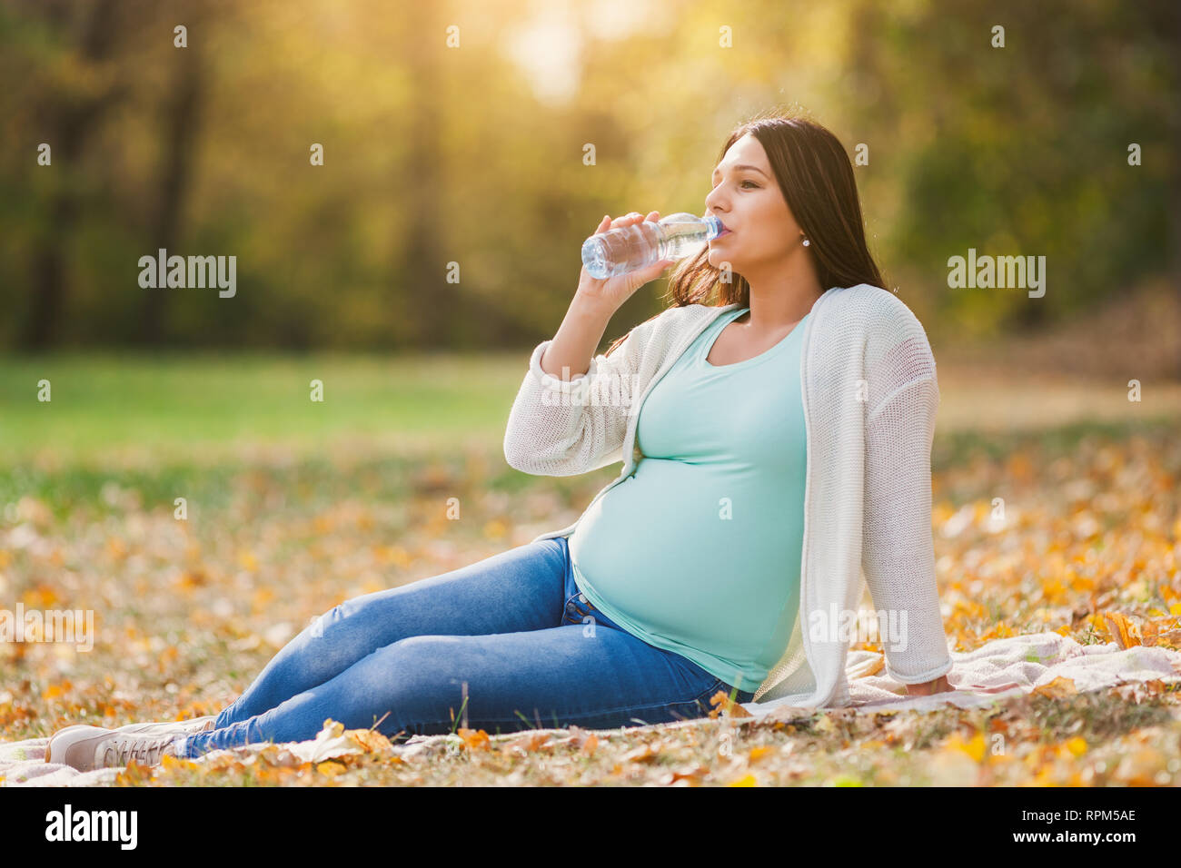 Schwangere Frau im Park. Sie ist Trinkwasser. Stockfoto