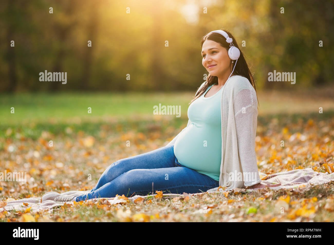 Schwangere Frau im Park. Sie ist Musik hören. Stockfoto