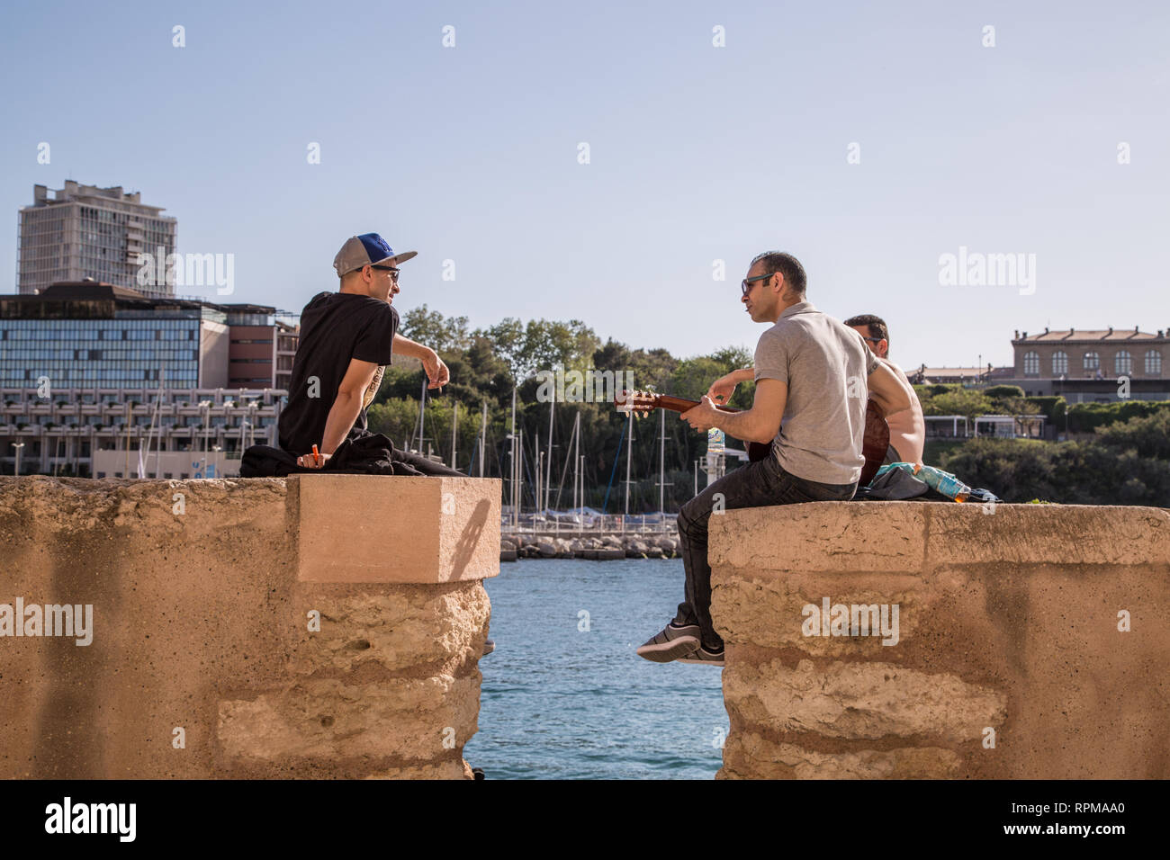 Eine Gruppe Männer entspannen und Musik wiedergeben, während Sie sitzen auf der Mauer des Vieux Port (alter Hafen) Marseille, Frankreich, an einem warmen Sommertag. Stockfoto