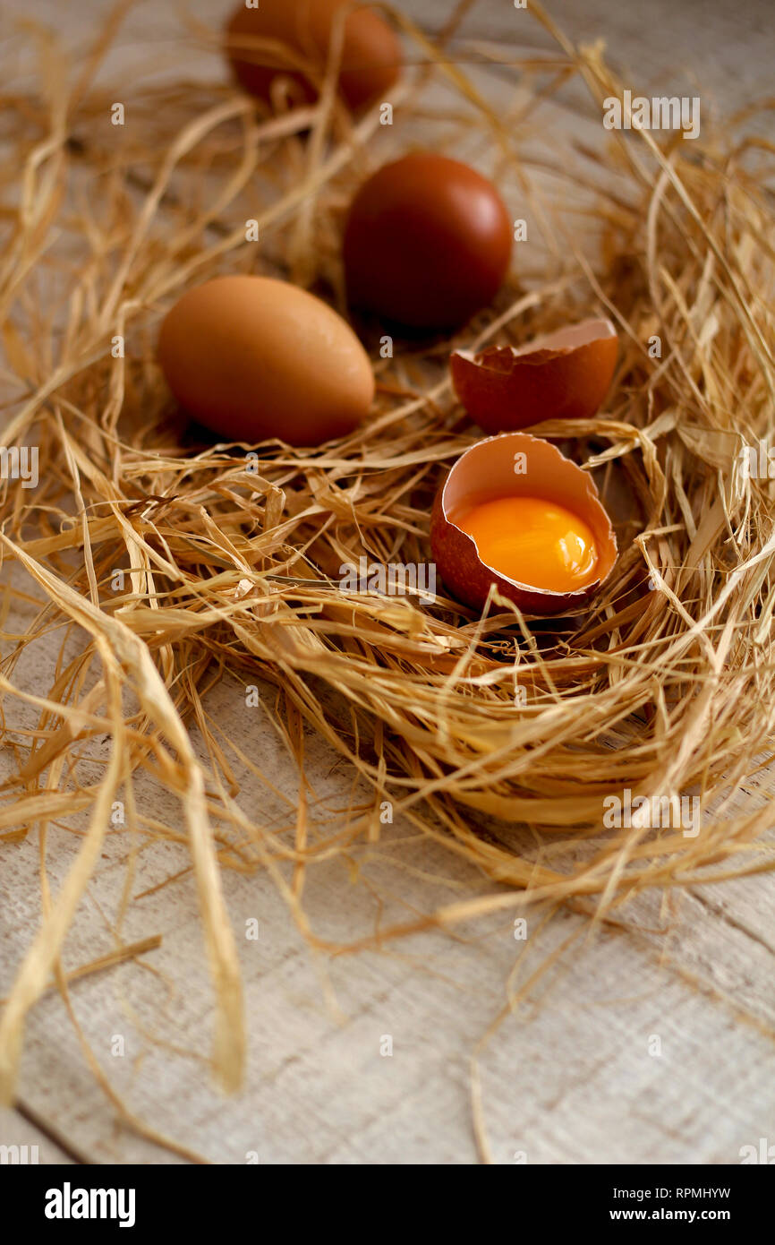 Eine Gruppe von Eiern und einem zerbrochenen Ei im Heu auf einem Holztisch Stockfoto