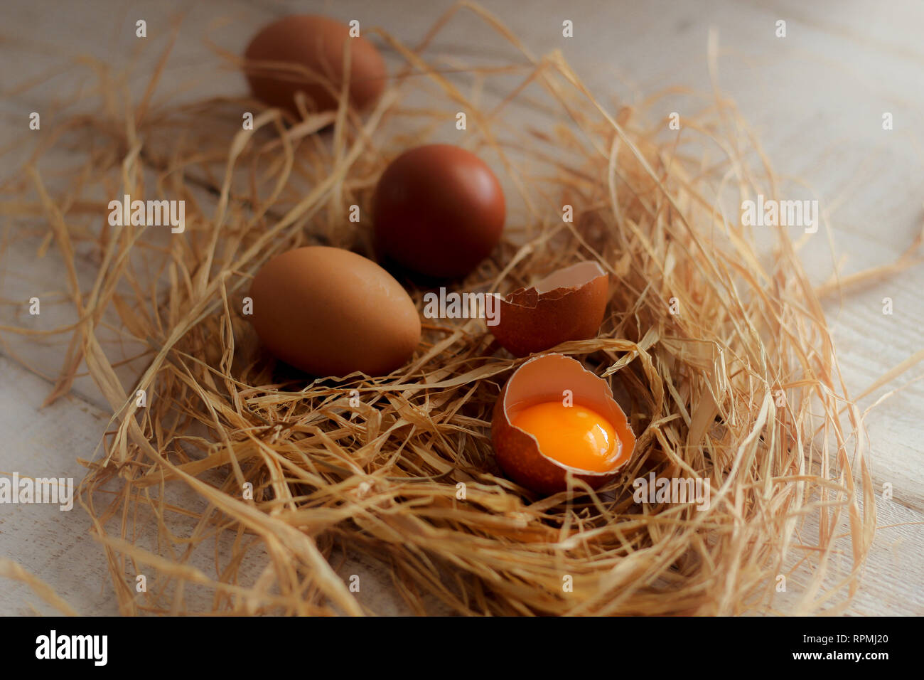 Eine Gruppe von Eiern und einem zerbrochenen Ei im Heu auf einem Holztisch Stockfoto