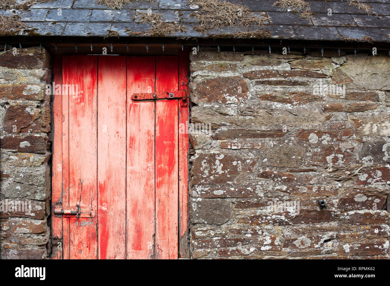 Rot und Distressed Holztür auf eine alte Scheune mit Schiefer Ziegeldach Stockfoto