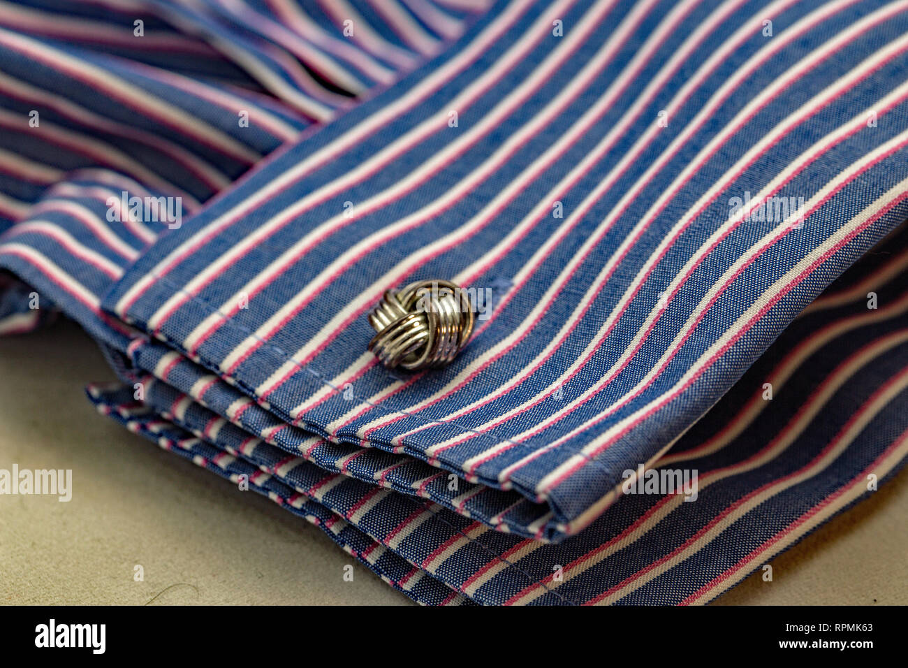 Nahaufnahme von einem keltischen Knoten design Metall Manschettenknöpfe umklammern die doppelte Manschette eines gestreiften Fashion Shirt. Stockfoto