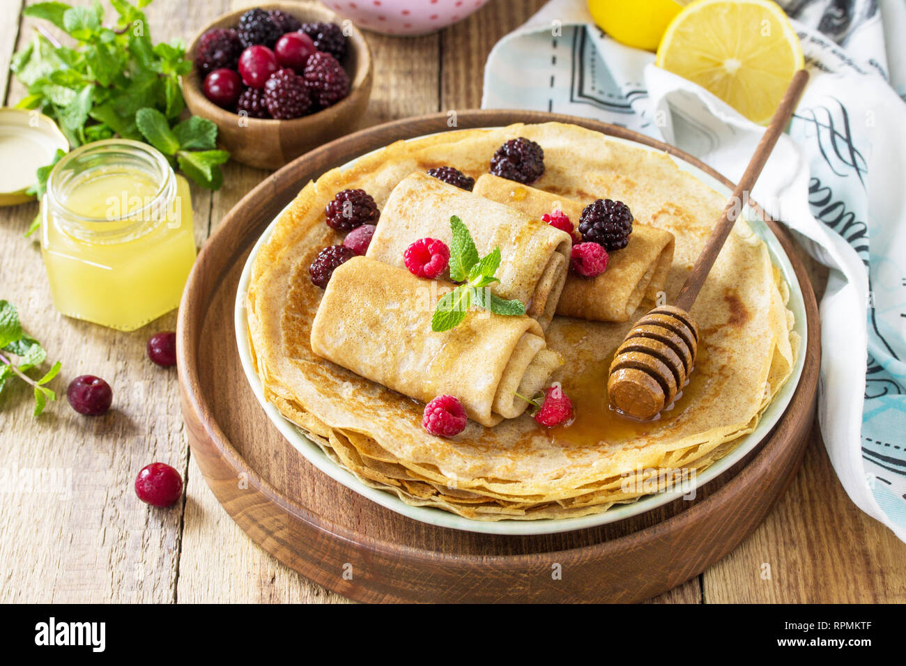 Gesunde Pfannkuchen Frühstück. Stapel von hausgemachten dünne Pfannkuchen oder Crepes auf einer rustikalen Tisch, mit Honig und frischen Beeren serviert. Stockfoto
