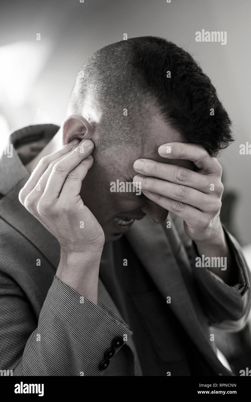 Nahaufnahme eines Leidens kaukasischen Mann mit einer Hand in seinem Kopf und mit der anderen Hand über sein Ohr Stockfoto
