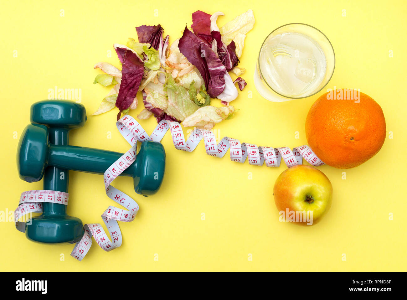 Hanteln für Sport. Fitness Salat und Maßband auf einem gelben Tabelle. Orangen, Äpfel und klares Wasser mit Eis für das Konzept einer gesunden lifestyl Stockfoto