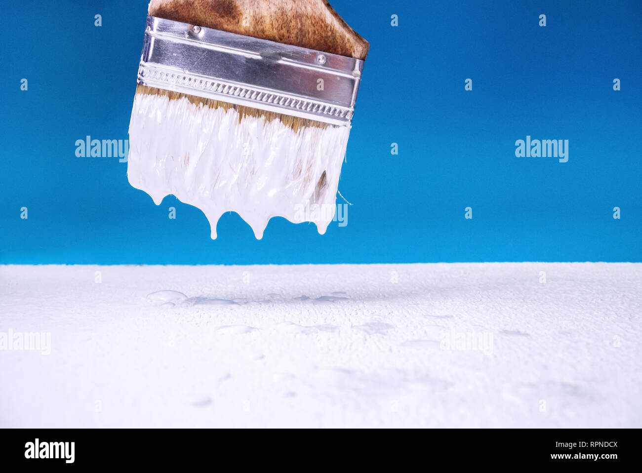 Mit einem Pinsel tropft weiße Farbe auf der Oberfläche der Malerei. blauen Hintergrund. Stockfoto