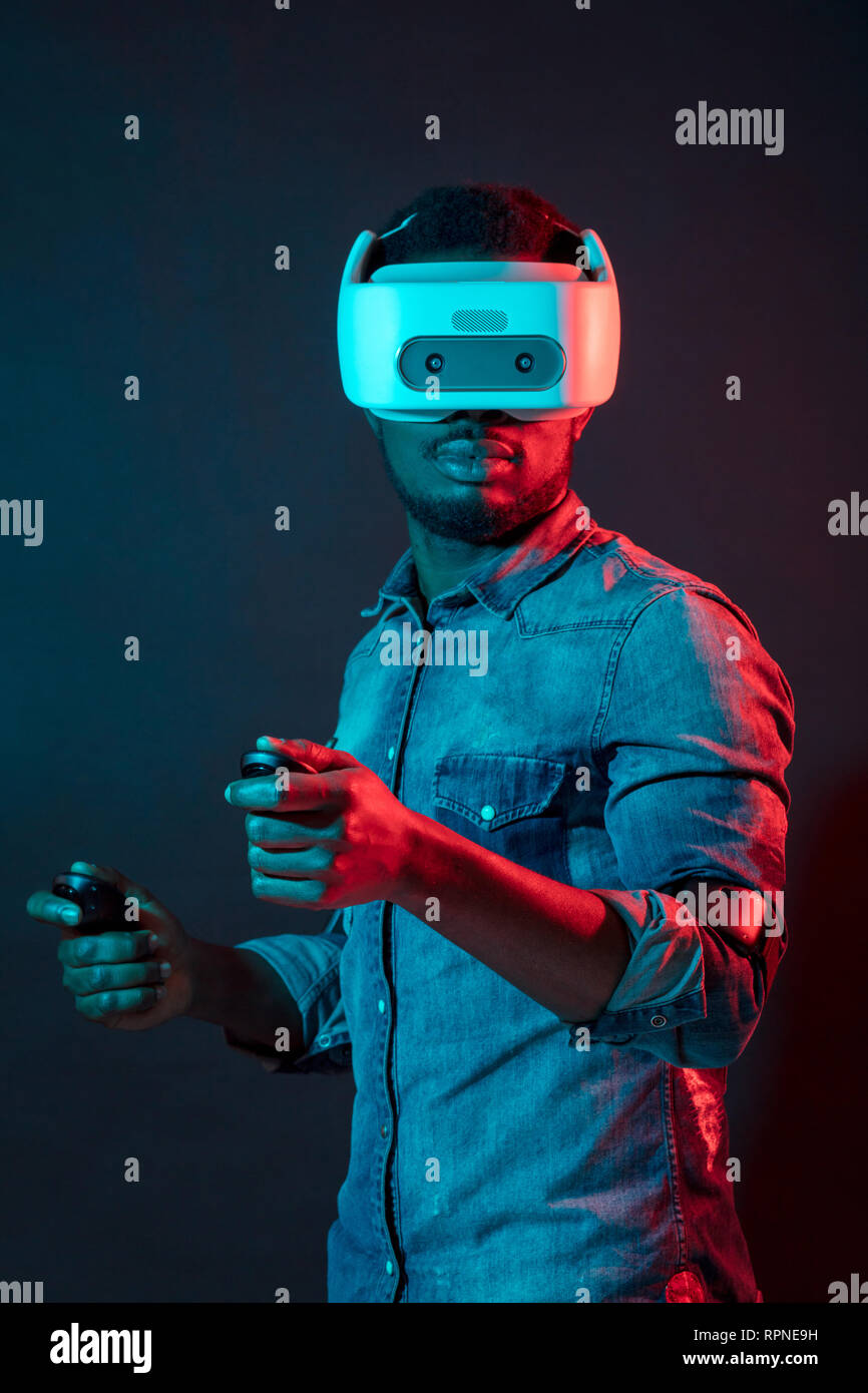 Video Spiel männlichen Designer tragen VR-Headset und Betrieb mit Gamepads seine neue Bilder in der virtuellen Realität zu sehen, sich gegen Rot und Blau dual Stockfoto