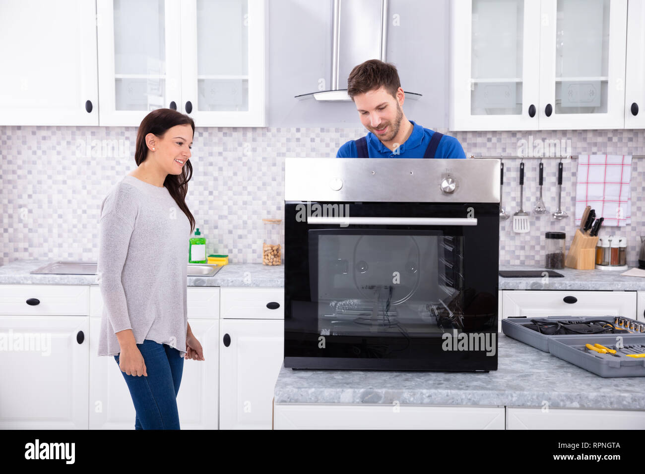 Lächelnd Handwerker Instandsetzung Backofen auf der Küchenarbeitsplatte Vor Frau Stockfoto