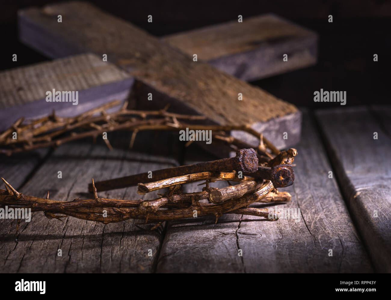 Dornenkrone und Nägel auf eine rustikale Holz- Oberfläche mit einem hölzernen Kreuz im Hintergrund Stockfoto