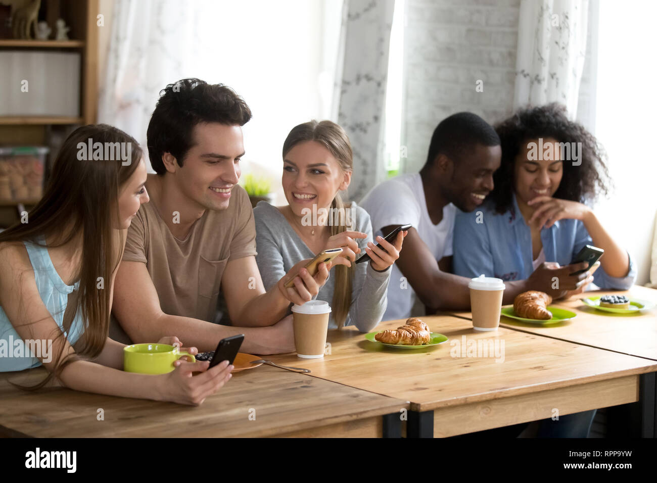 Glücklich lächelnde Freunde sitzen zusammen im Café, über Telefone Stockfoto