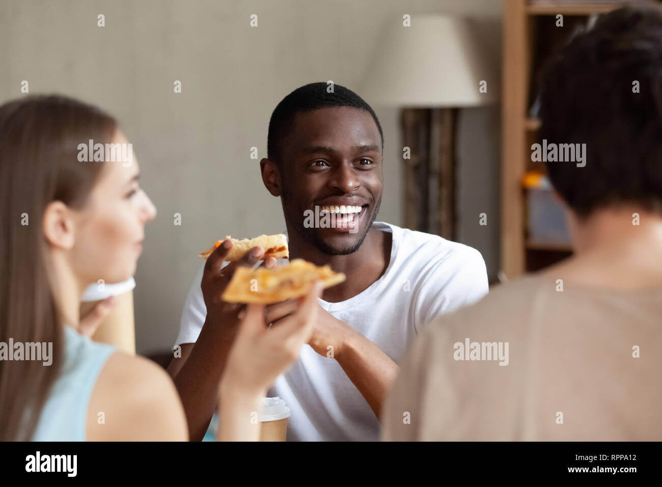 Lächelnd afrikanische amerikanische Mann essen Pizza, mit Freunden chatten Stockfoto