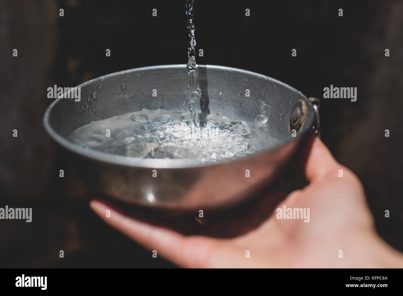 Hände Sammeln von Wasser aus Brunnen mit Metall Schüssel Stockfoto