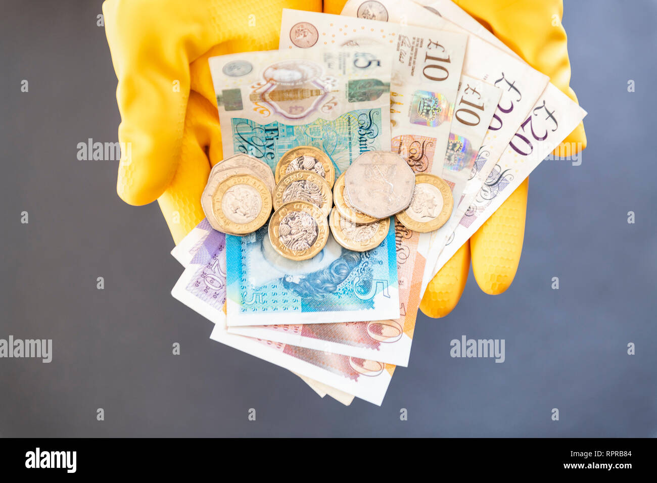 Ein paar Hände tragen gelbe Gummihandschuhe holding Pfund Noten und Münzen. Konzept Kassenbestand, Schwarzarbeit oder niedrige Zahlen. Stockfoto