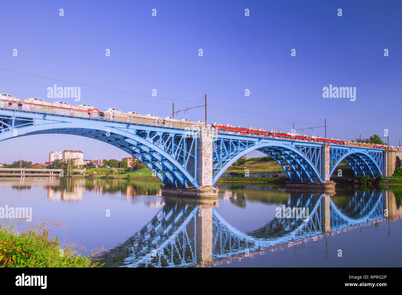 Güterzug Autos schleppen auf Blue Steel Eisenbahnbrücke über den Fluss Drawa. Cargo Bahn, Eisenbahn. Spiegelungen im Wasser. Maribor, Slowenien. Stockfoto