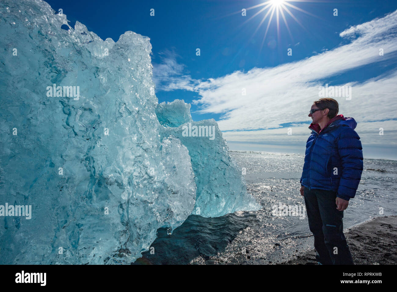 Person, die die Prüfung eines Eisberg auf Breidamerkursandur schwarzer Sandstrand, unter Jokulsarlon ist. Sudhurland, South East Island. Stockfoto