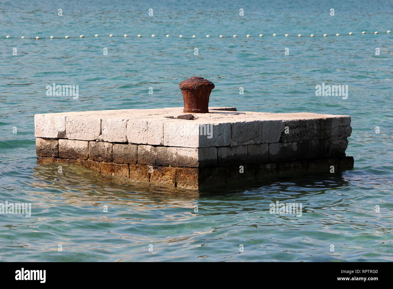 Komplett verrostet verfallenen Bügeleisen bootsanlegeplatz Poller in der Mitte der steinernen Pier mit ruhigen Meer auf allen Seiten für das Binden der größeren Schiffen umgeben Stockfoto