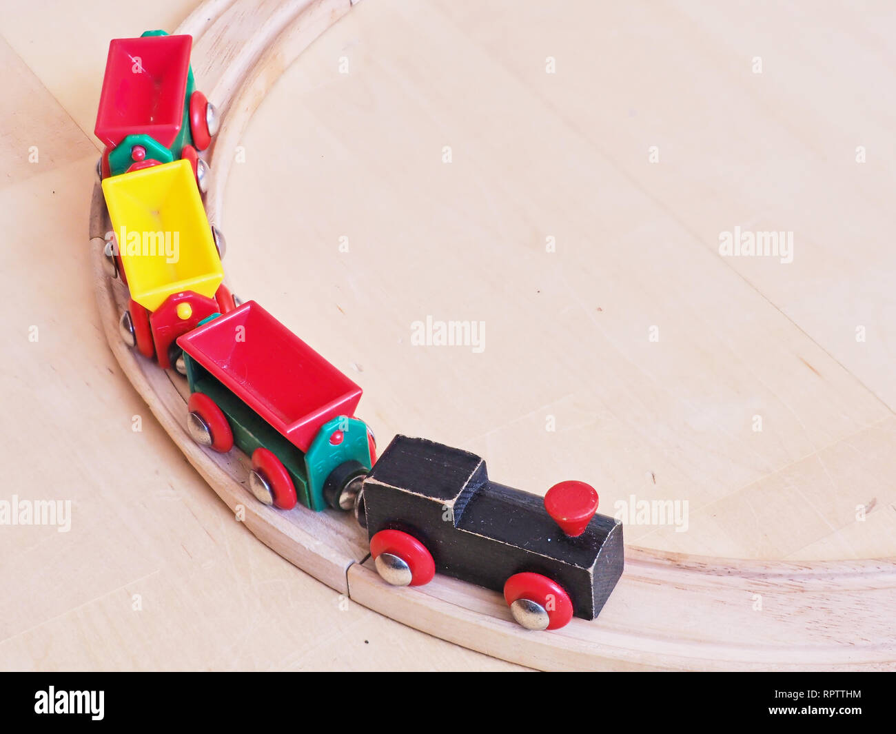 Holzspielzeug Zug, der auf miniatur Eisenbahnschienen. Die schwarzen Motor ziehen bunte Autos auf dem Boden. Pädagogische Spielwaren für Kinder im Vorschulalter Stockfoto
