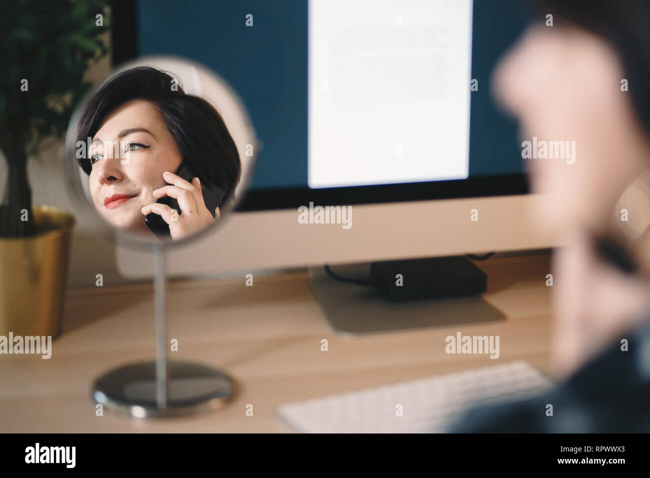 Reflexion eines weiblichen Geschäftsfrau in einem Kosmetikspiegel, sprechen über Ihr Mobiltelefon und Arbeiten im Home Office. Stockfoto