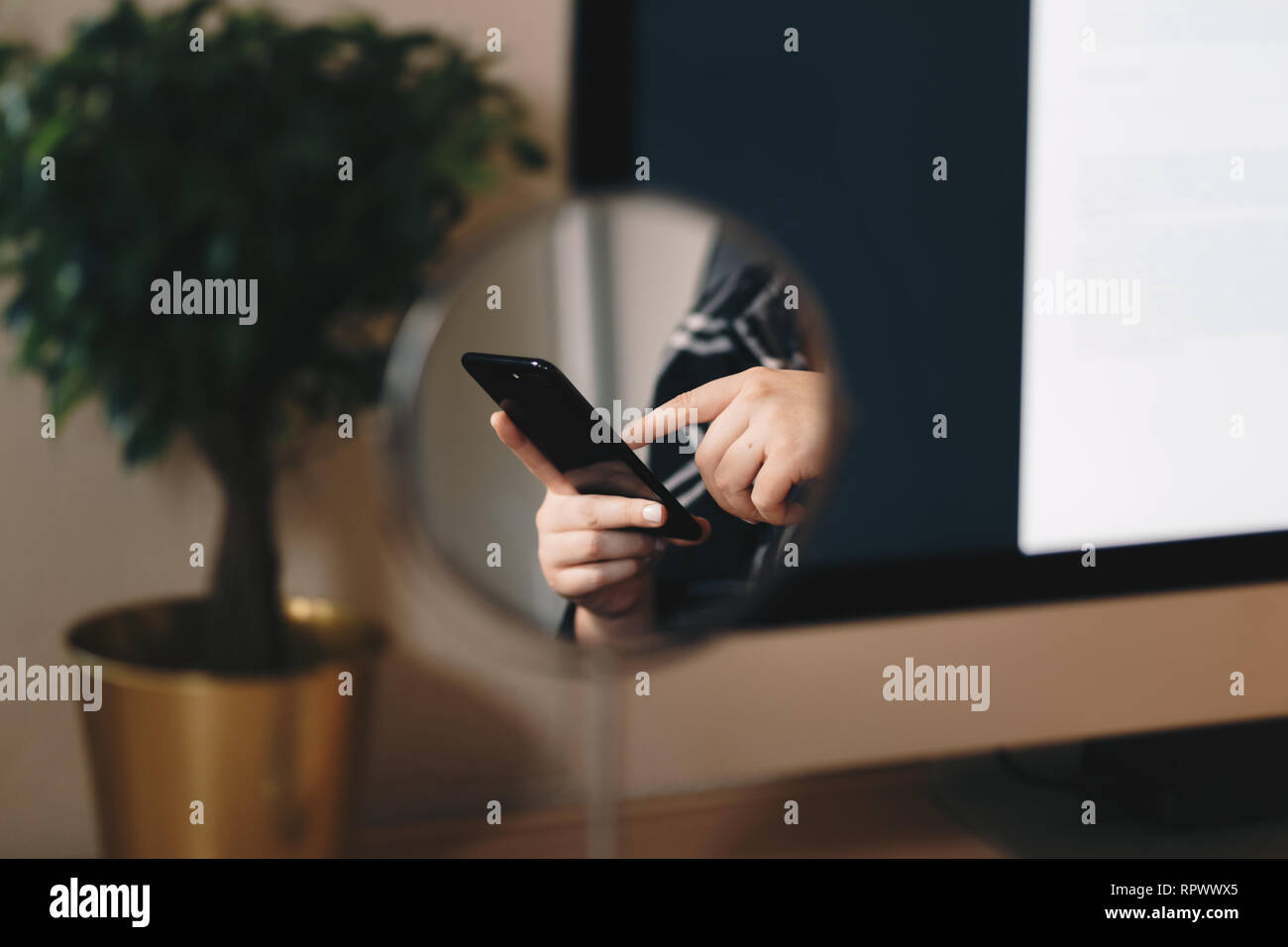 Detail Aufnahme der Hand einer Frau, die in einer Reflexion der einen Kosmetikspiegel. Texteingabe auf einem smart phone im Home Office wie Raum. Stockfoto